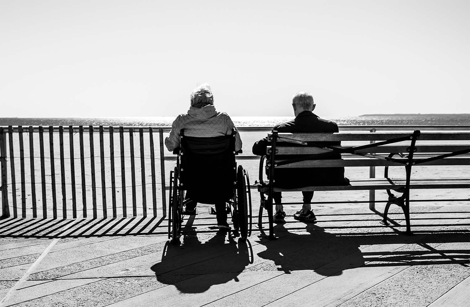 Black and white image of two elderly people sat by the sea