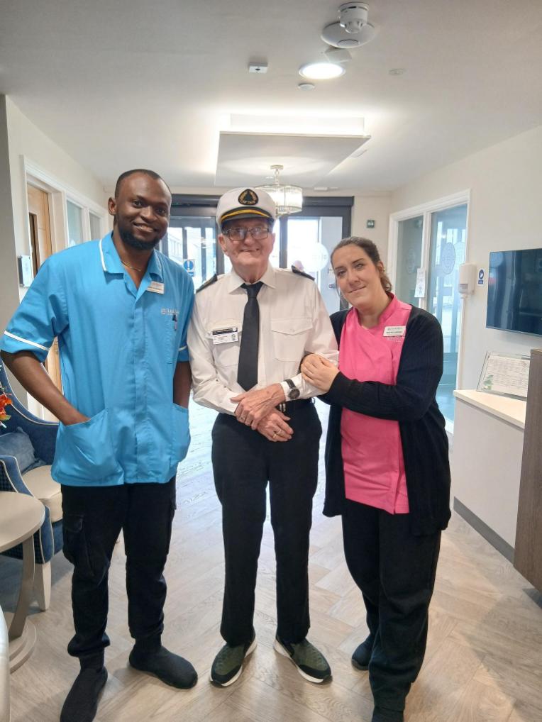 resident in his navy uniform with staff at the care home