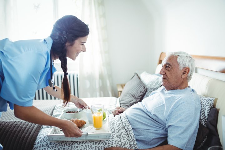 nurse giving resident his breakfast in bed